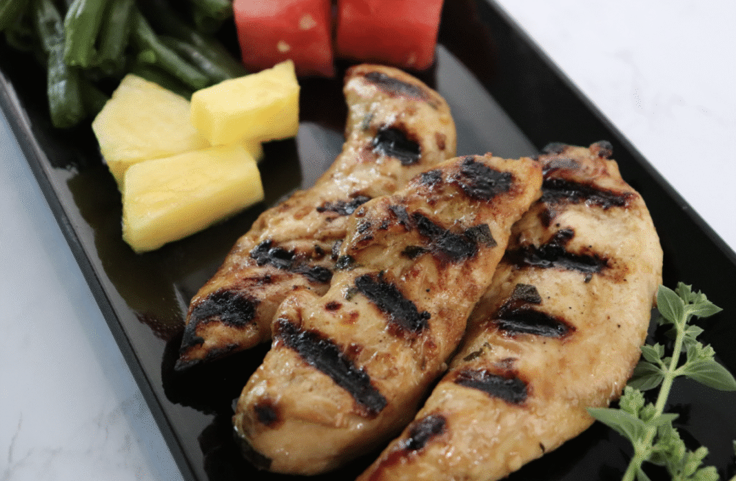 Grilled marinated chicken tenderloins on a black serving platter with fresh thyme.