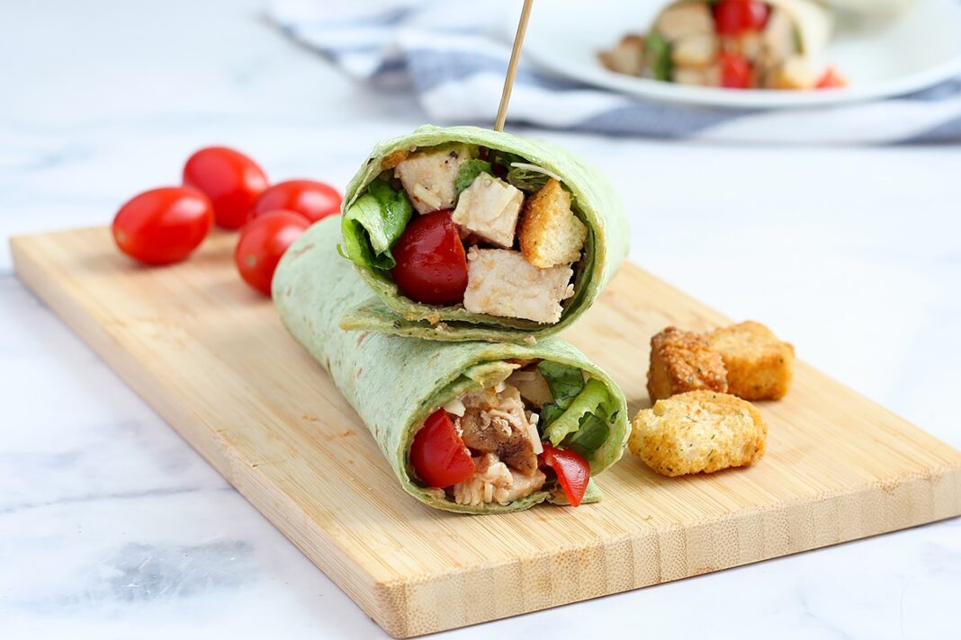 chicken caesar wraps on a wooden board with grape tomatoes and croutons