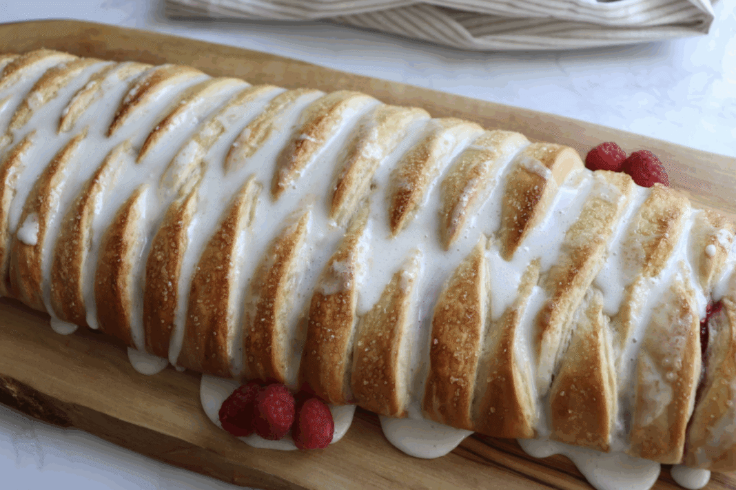 raspberry cream cheese braided bread topped with a vanilla glaze displayed on a wooden cutting board