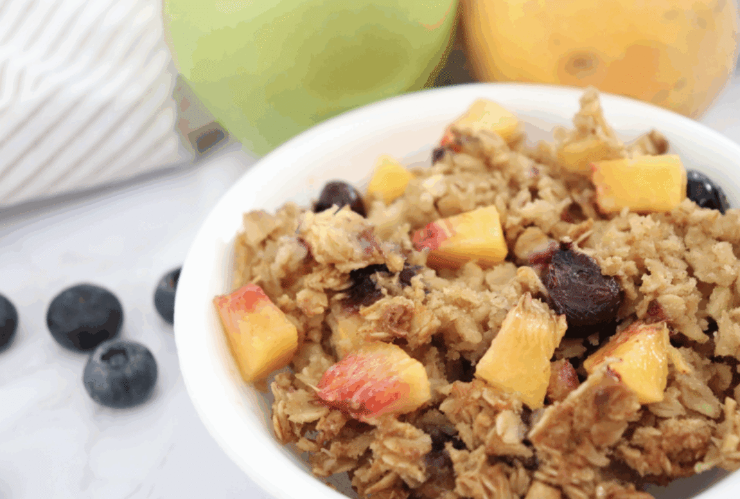 Fruity baked oatmeal in a white serving bowl with fresh blueberries and apples in the background.