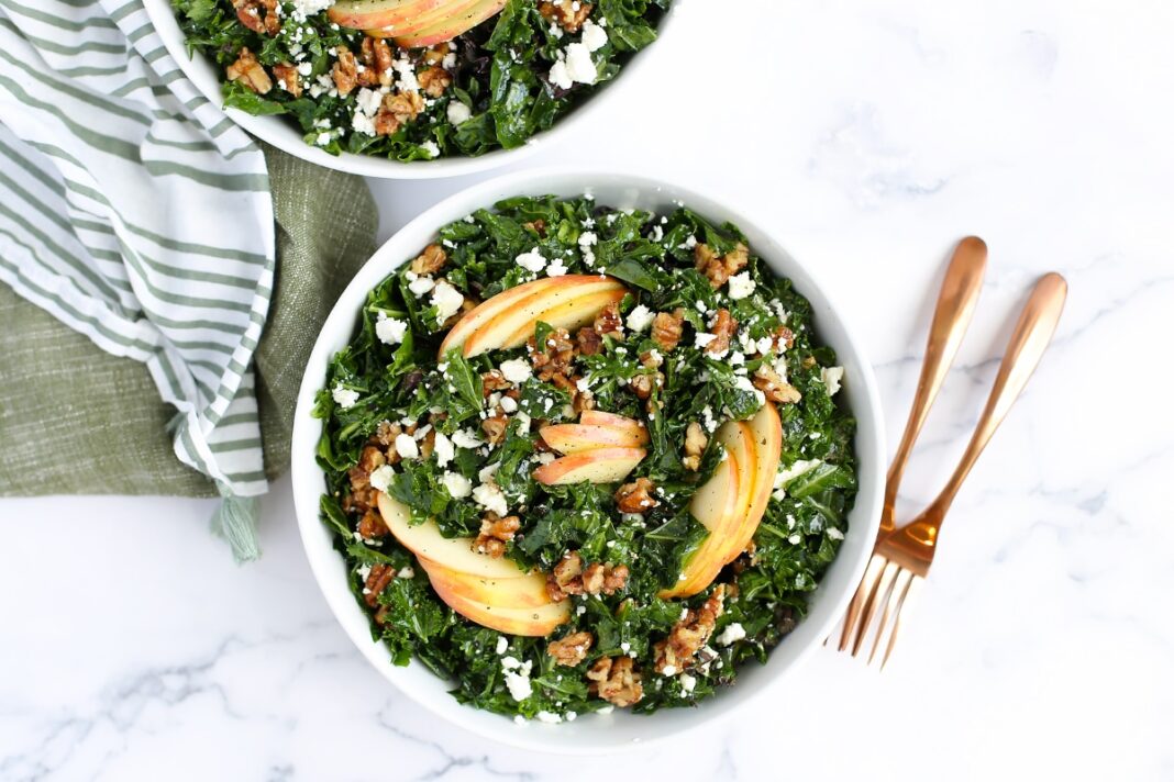 massaged kale salad with apples in white serving bowls with a striped linen in the background