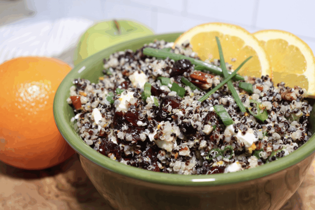 cranberry quinoa salad topped with green onions and orange slices in a green serving bowl