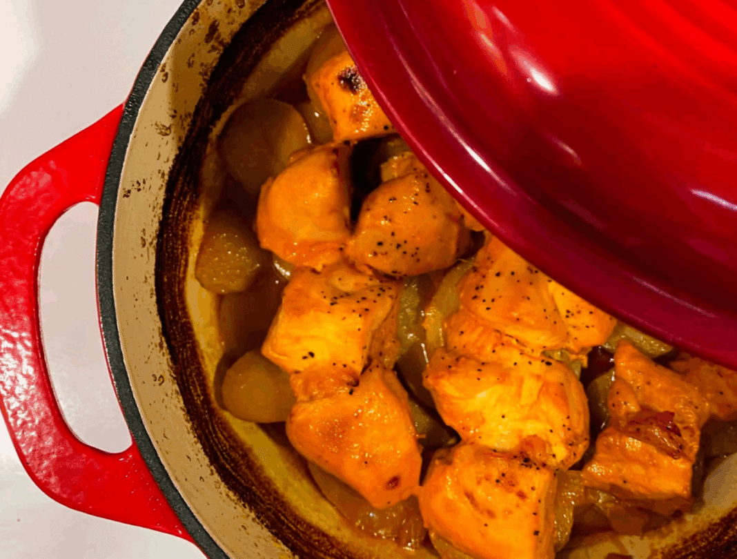 dutch oven chicken in a red cast iron pot with onions and potatoes