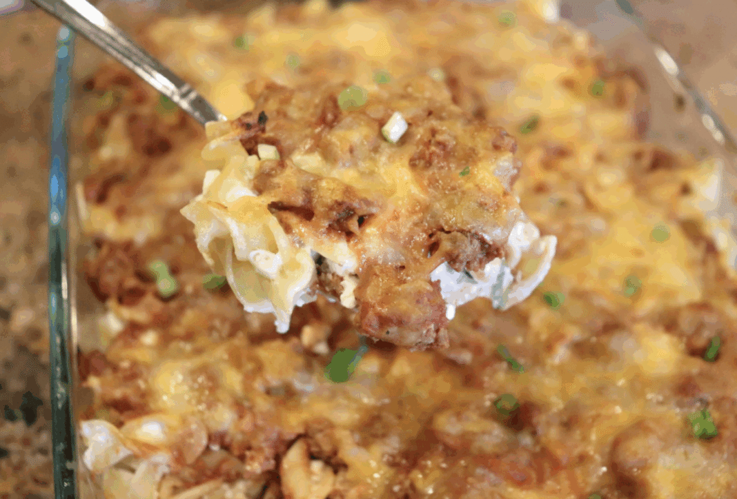 noodle casserole in a glass dish being scooped out with a serving spoon