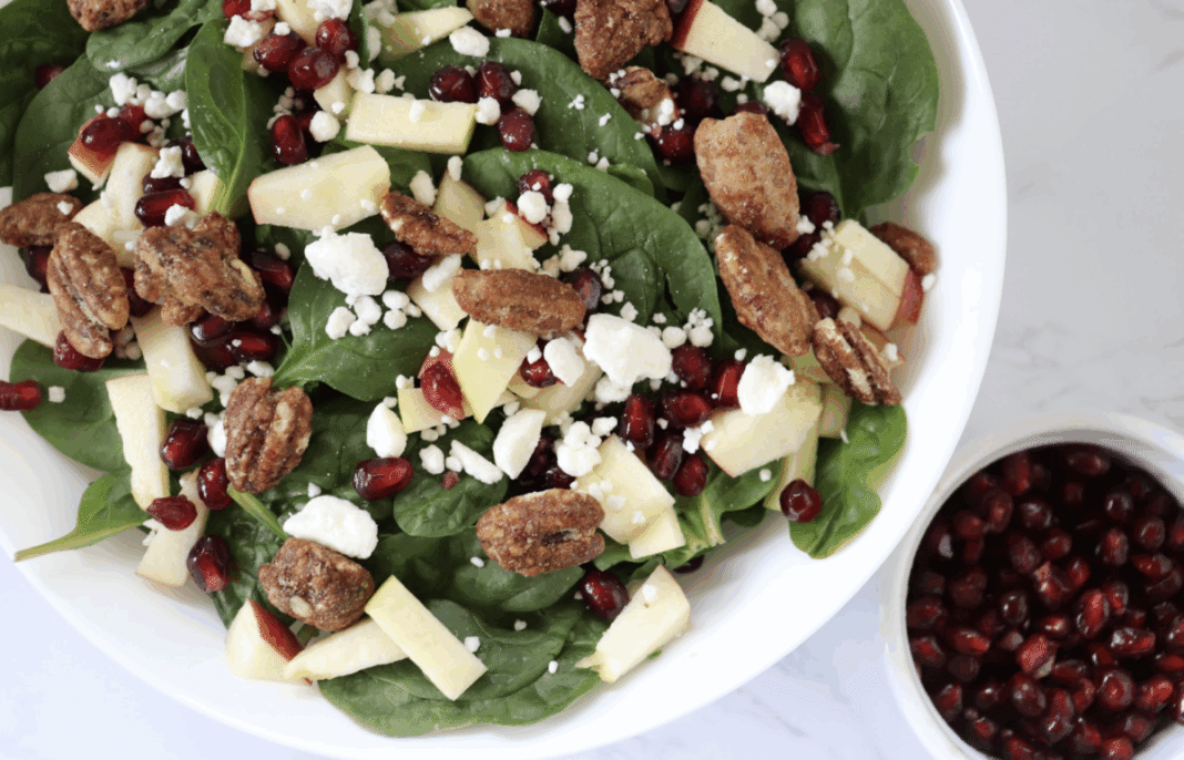 holiday spinach salad with apples, feta, and pomegrante in a serving bowl