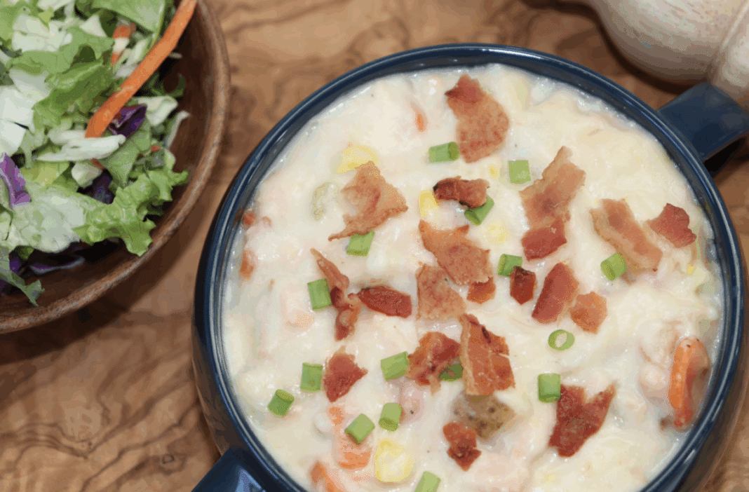 salmon chowder with bacon bits and green onions in a serving bowl on a wooden platter